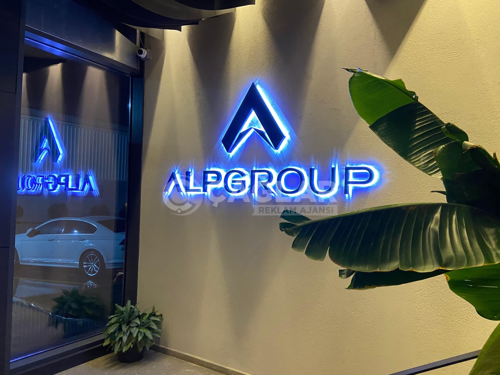 Alpgroup giriş duvarında mavi ışıklı kabartma logo ve kutu harfler